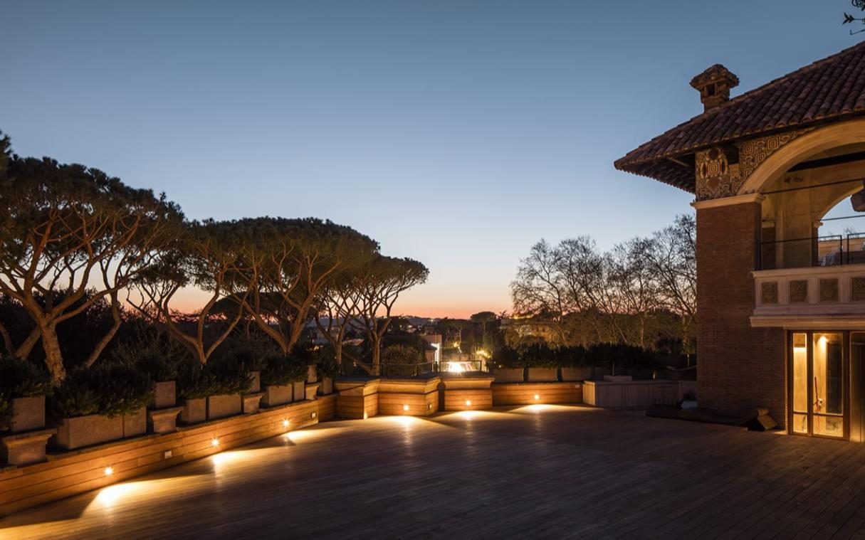 Villa Clara — the lantern-lit roof terrace at dusk, umbrella pines beyond · Rome, Italy